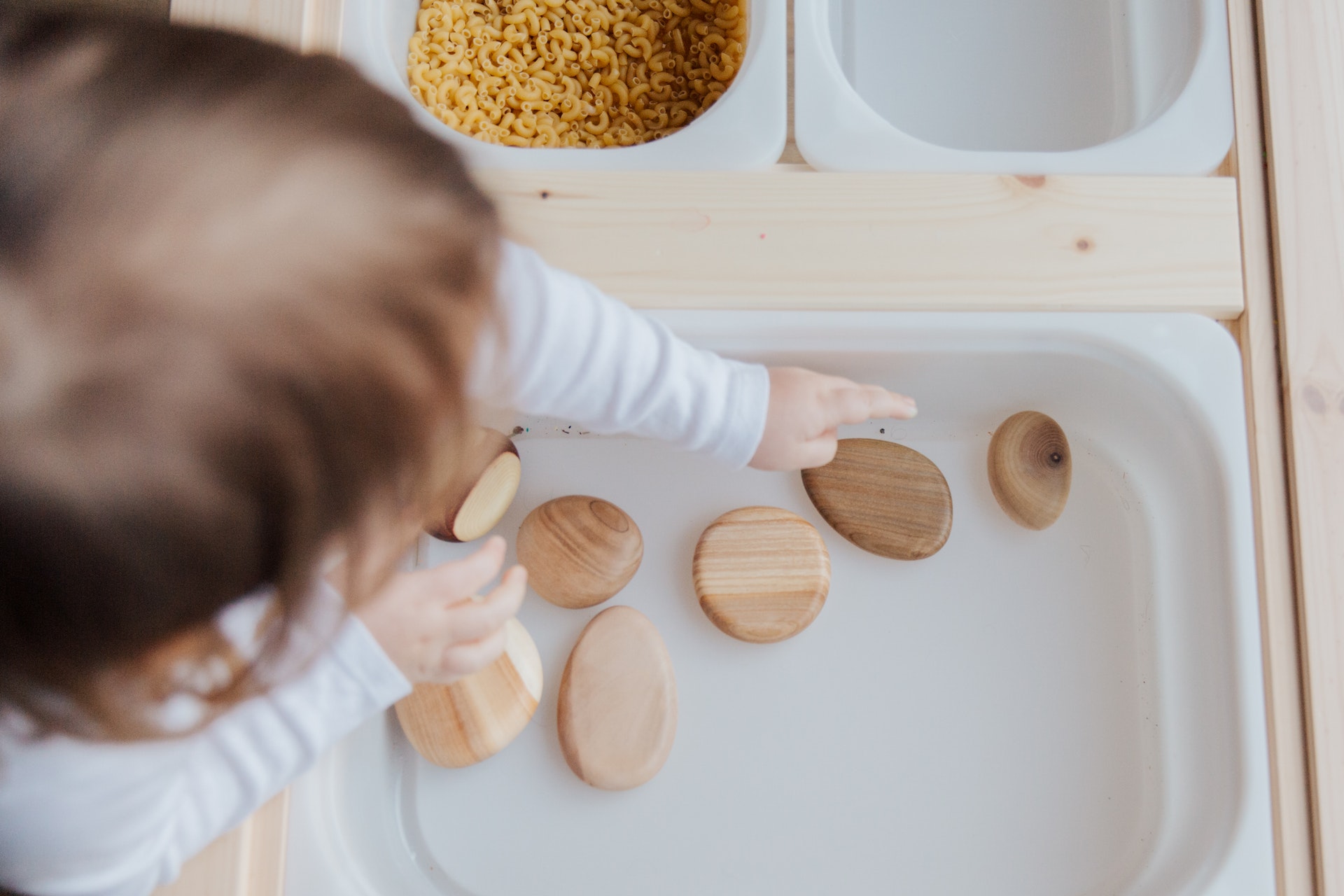 Baby exploring smooth wooden pieces on a white tray