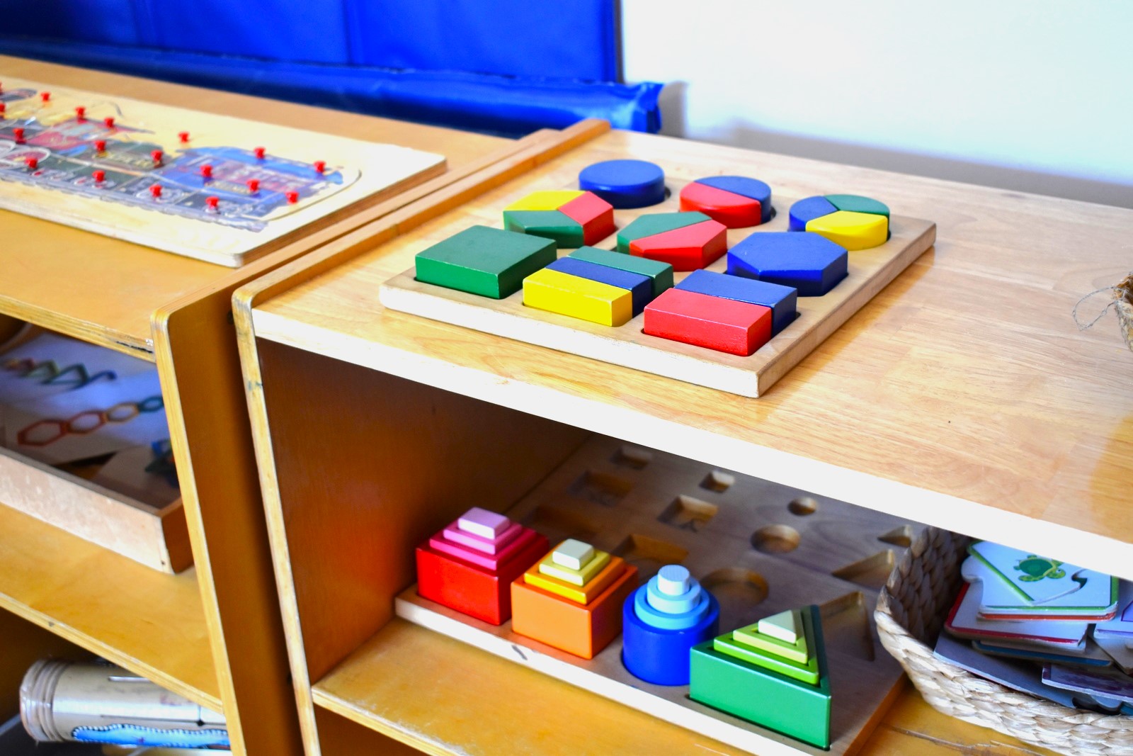 Montessori sensorial materials in bright colours on a low classroom shelf